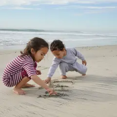Dzieci tworzą budowle z piasku na plaży, rysując palcami wzory w mokrym piasku.