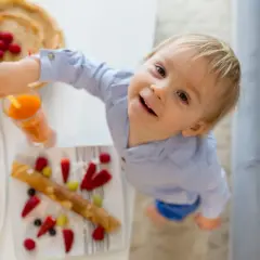 Uśmiechnięty maluch sięga po pyszne naleśniki dla niemowlaka, obok owocowa sałatka i sok.
