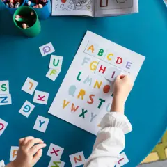 Dziecko układa kolorowe, pisane litery polskie na niebieskim stole, ucząc się alfabetu.