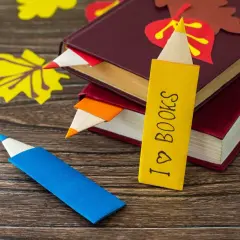 Kolorowe zakładki do książek ręcznie robione przez dzieci, w kształcie kredek. Jedna z nich z napisem "I ♡ BOOKS".
