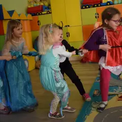Dzieci w strojach księżniczek i kota bawią się w przeciąganie liny. Wesołe zabawy karnawałowe dla dzieci pełne śmiechu i rywalizacji.