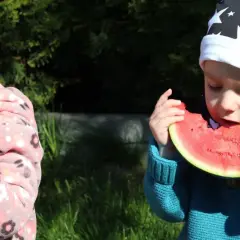 Dwa maluchy w czapkach zajadają soczystego arbuza. To idealny arbuz dla niemowlaka na letnie orzeźwienie.