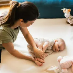 Mama bawi się z niemowlakiem na macie. Uśmiechnięty maluch leży obok pluszowej żyrafy i królika.