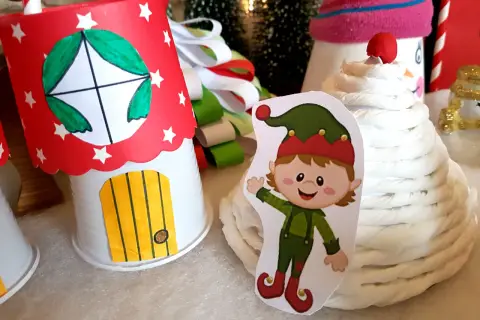 Uroczy elfik obok domku z papieru, jak z bajki. Idealne do stworzenia własnych sanie Mikołaja do druku.