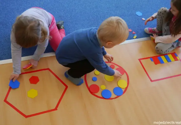 Dzieci układają kolorowe figury geometryczne, tworząc wzory w wyznaczonych obszarach.