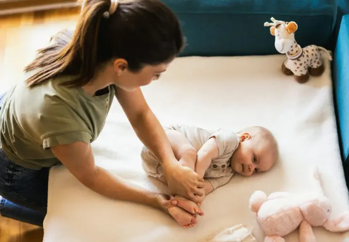 Mama bawi się z niemowlakiem na macie. Uśmiechnięty maluch leży obok pluszowej żyrafy i królika.