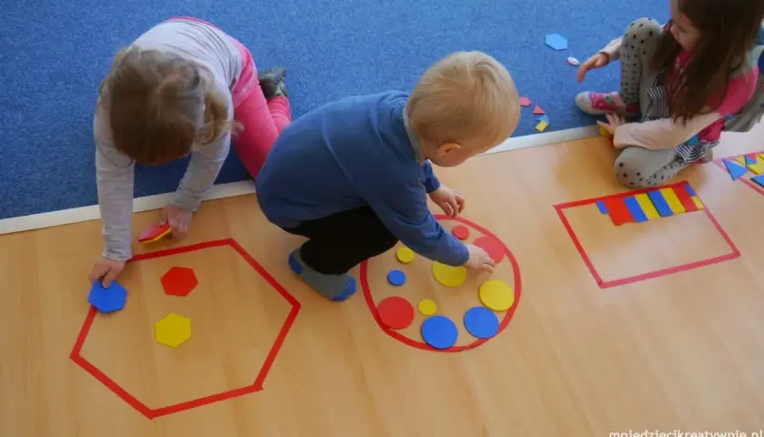 Dzieci układają kolorowe figury geometryczne, tworząc wzory w wyznaczonych obszarach.