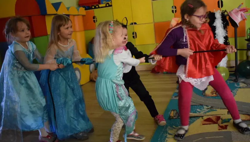Dzieci w strojach księżniczek i kota bawią się w przeciąganie liny. Wesołe zabawy karnawałowe dla dzieci pełne śmiechu i rywalizacji.