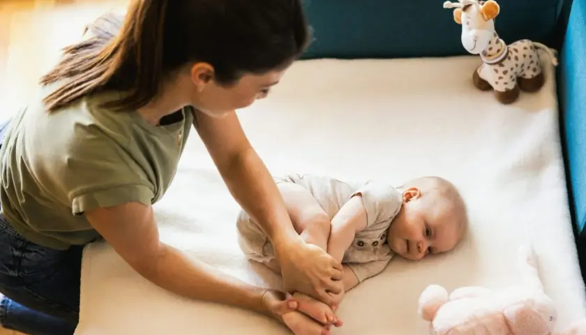 Mama bawi się z niemowlakiem na macie. Uśmiechnięty maluch leży obok pluszowej żyrafy i królika.