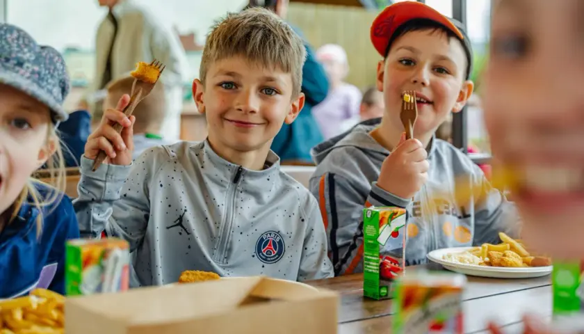 Uśmiechnięci chłopcy jedzą frytki i nuggetsy, świetne pomysły na warsztaty dla dzieci.