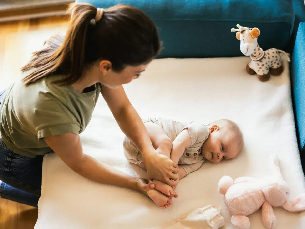 Mama bawi się z niemowlakiem na macie. Uśmiechnięty maluch leży obok pluszowej żyrafy i królika.