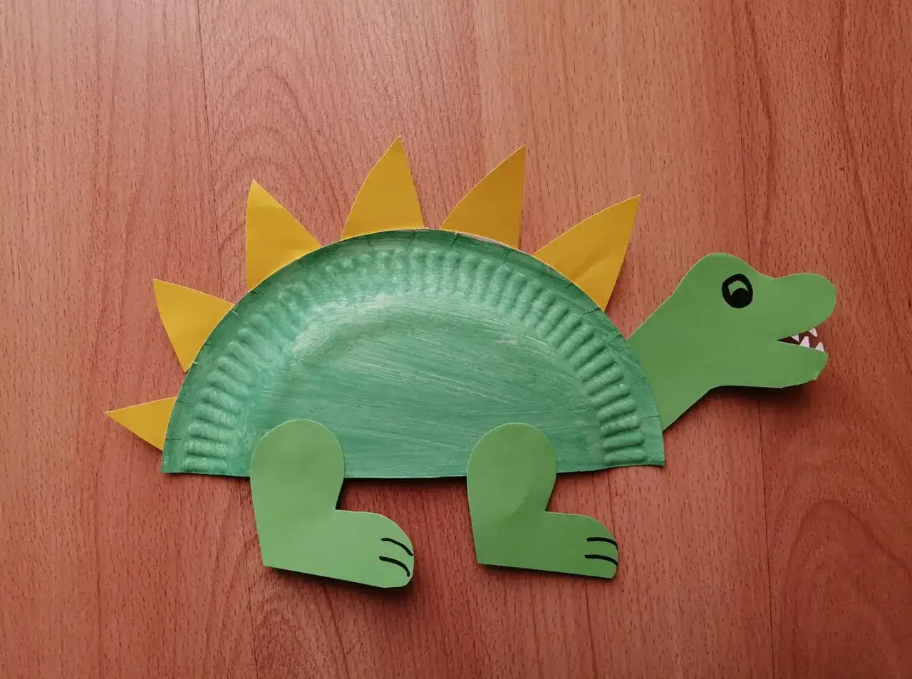 Zielony dinozaur z papierowego talerzyka, ozdobiony ż&oacute;łtymi kolcami. Urocza dinozaur praca plastyczna.